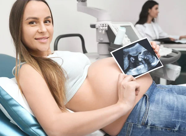 Mother showing ultrasound screen of future baby in clinic