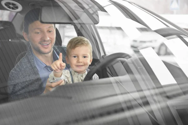 Boy and father sitting in car and laughing in auto salon — Stock Photo, Image