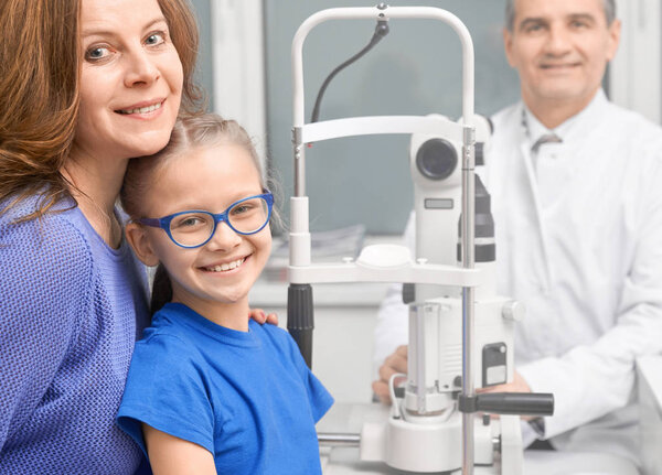 Patients smiling, posing with ophthalmologist in clinic.