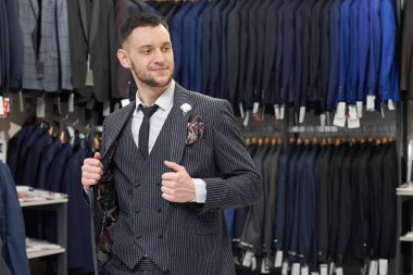 Butikte alışveriş yapan, gri şık takım elbiseyi deneyen adam.