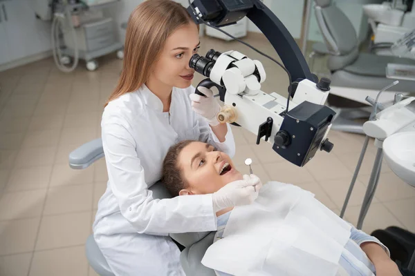 Dentysta patrząc przez dentystyczny Mikroskop u zęby. — Zdjęcie stockowe