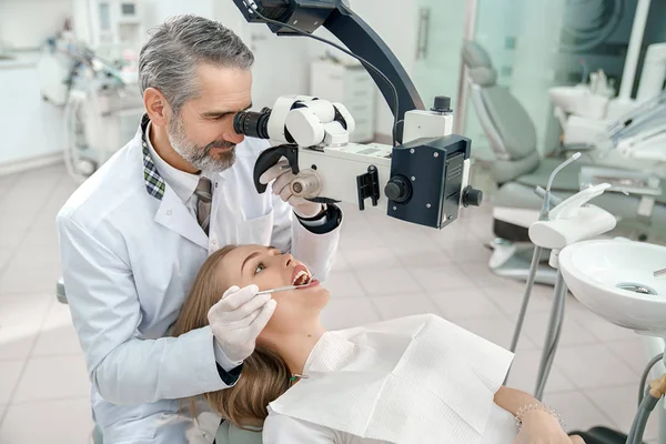 Erkek diş hekimi mikroskoba bakıyor ve dişleri kontrol ediyor — Stok fotoğraf