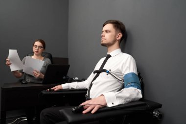 Kadın adamı gri odada yalan makinesiyle test ediyor..