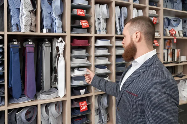 Barbudo cliente masculino de pé perto racks com roupas — Fotografia de Stock