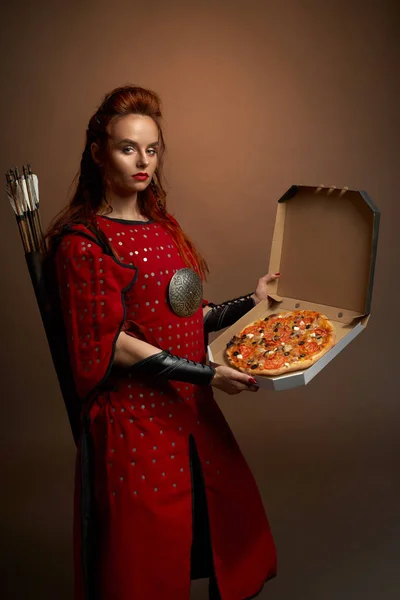 Female fighter in armor keeping pizza on isolated background