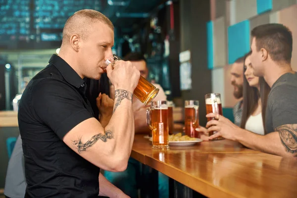 Homem tatuado forte sentado bebendo cerveja no pub — Fotografia de Stock