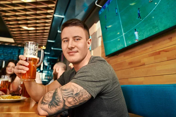Csinos férfi nézi a kamerát, miközben sört iszik — Stock Fotó