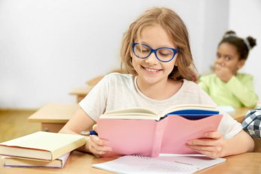 Mutlu kız öğrenci masada kitap bakarak, gülümseyerek okuyan.