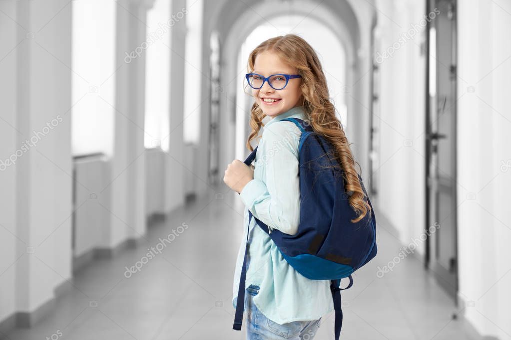 Schoolgirl with backpack posing, looking at camera.