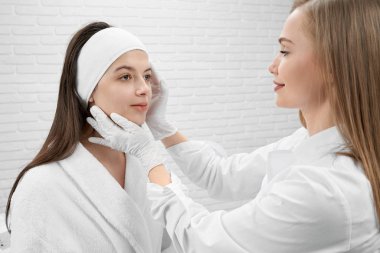 Eldivenlerde kozmetoloji uzmanı müşterinin yüzünü teftiş, dokunma.