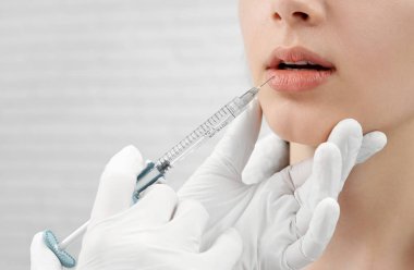 Kadın dudaklarında enjeksiyon yapan tıbbi eldiven eller.