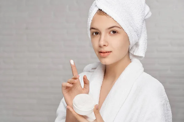 Menina segurando e mostrando creme para o cuidado do rosto da pele . — Fotografia de Stock