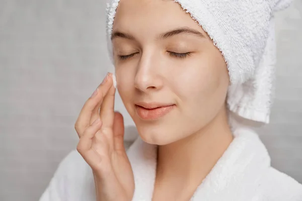 Woman with closed eyes applying moisturizer on face. — Stock Photo, Image