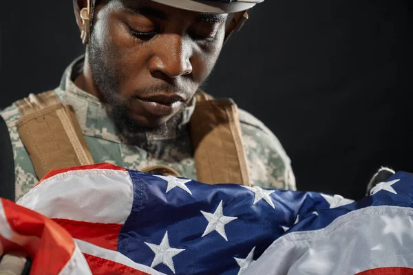 Soldaat in helm helaas kijken naar nationale vlag. — Stockfoto