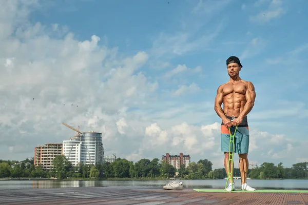 Hombre deportivo con pecho desnudo haciendo ejercicio en el muelle del lago . — Foto de Stock