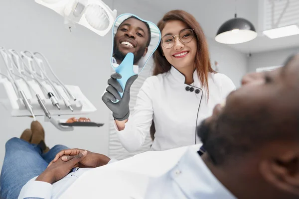 Dentista manteniendo espejo y mostrando una sonrisa blanca al paciente —  Fotos de Stock