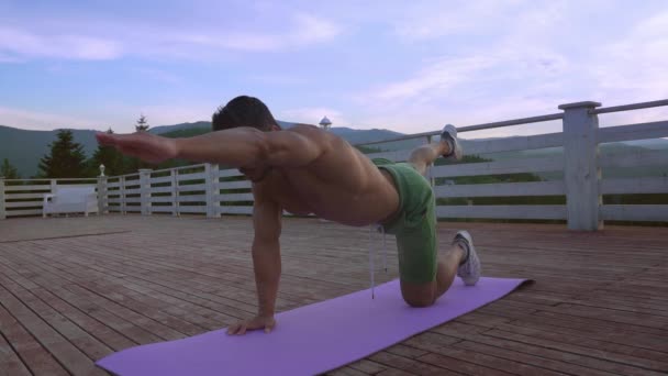 Молодий сильний чоловік тягнеться на фіолетовий йога мат на відкритому повітрі — стокове відео