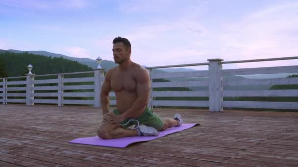 裸の筋肉の胴体を持つ男は、屋外で彼の足を伸ばす — ストック動画
