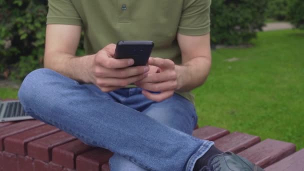 Close-up van de man handen met behulp van mobiele telefoon voor chatten in Park — Stockvideo