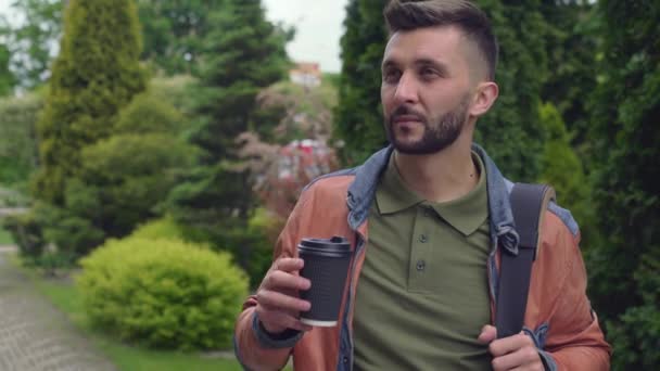 Pohledný stylový muž popíjí kávu v zeleném městském parku