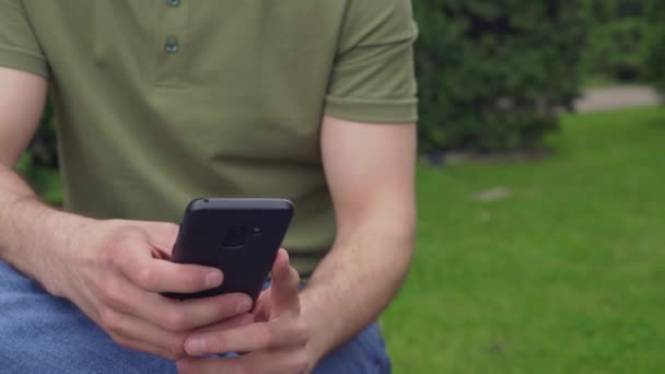 Primer plano de las manos de un hombre usando el teléfono móvil en el parque de la ciudad — Vídeos de Stock