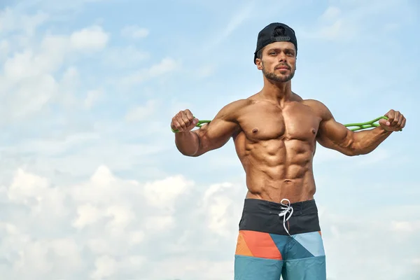 Musculoso, hombre fuerte con expansor en el fondo del cielo azul — Foto de Stock