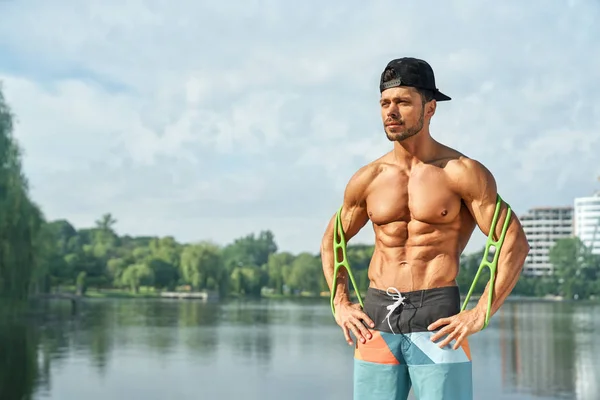 Homme musclé avec torse nu posant avec dilatateur à l'extérieur . Photo De Stock