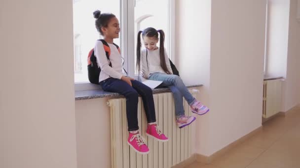 Två glada barn sitter på fönsterkarmen och skrattar — Stockvideo