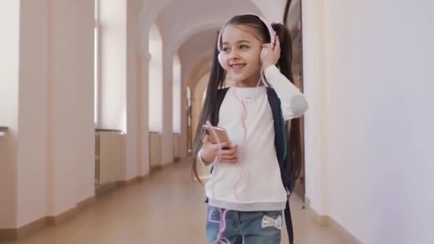 Chica feliz en los auriculares y escuchar música en la escuela — Vídeo de stock