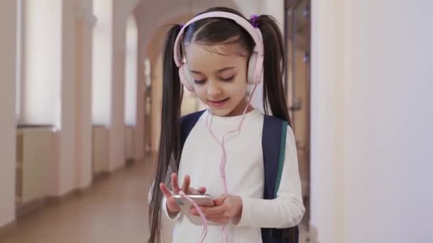 Chica bonita en auriculares rosados y escuchar música en la escuela — Vídeo de stock