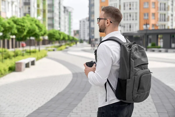 Young man walking with backpack and coffee cup in city. — Stock Photo, Image