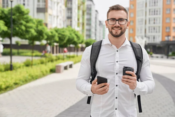 Hombre con mochila sosteniendo teléfono y taza de café negro . — Foto de Stock