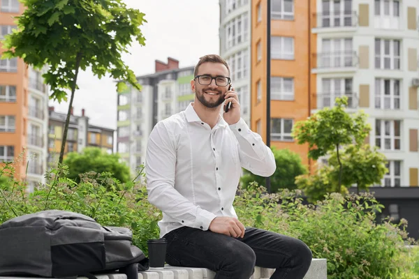 Man on bench, talking by phone, looking at camera, smiling. — Stock Photo, Image