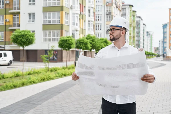 Hombre con proyecto arquitectónico sobre papel mirando casa . — Foto de Stock