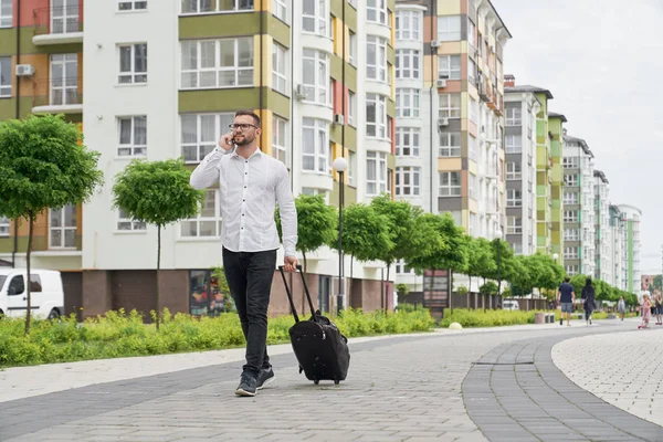 Pria dengan koper berjalan di jalan berbicara melalui telepon . — Stok Foto