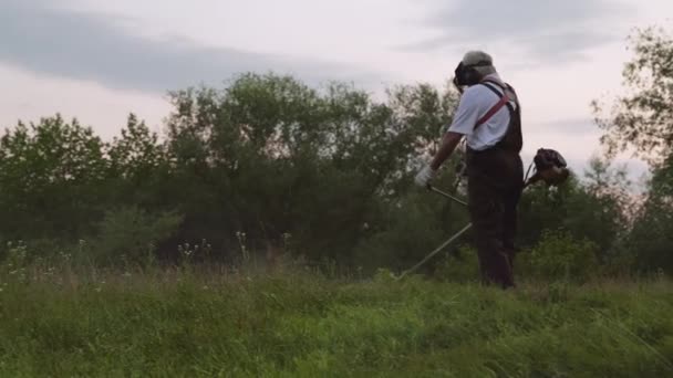 Mężczyzna pracownik wykorzystający elektryczny trymer i cięcie trawy — Wideo stockowe