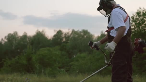 Мужчина в комбинезоне и защитная маска для стрижки травы — стоковое видео