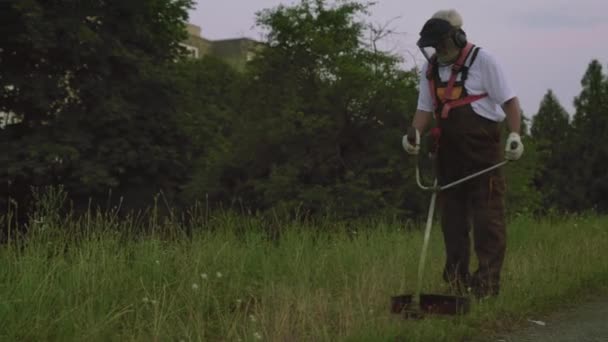 Вид сбоку на человека, использующего электрическую триммер и стригущего траву — стоковое видео