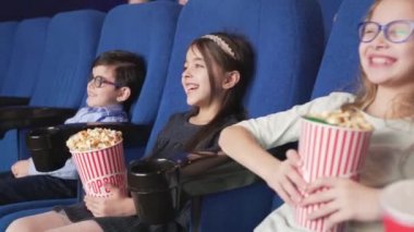 Sinemada rahat bir sandalyede oturan gülümseyen çocuklar grubu