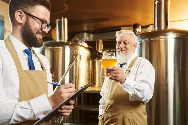 Dos cerveceros de pie en la cervecería y el examen de la calidad de la cerveza — Foto de Stock