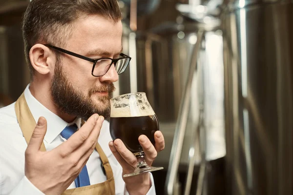 Primo piano dell'uomo barbuto in bicchieri che profuma di gustosa birra scura — Foto Stock