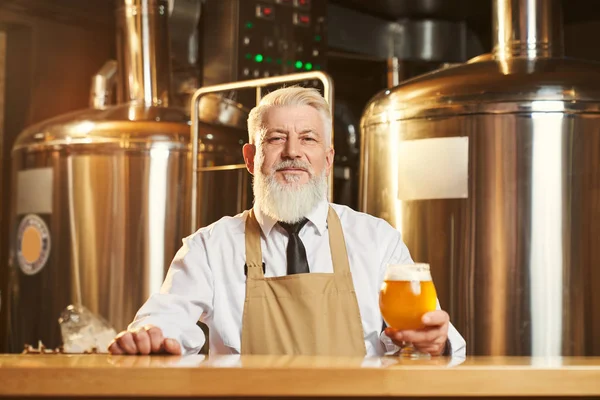 Vista frontal do cervejeiro em pé sobre bar com copo de cerveja — Fotografia de Stock