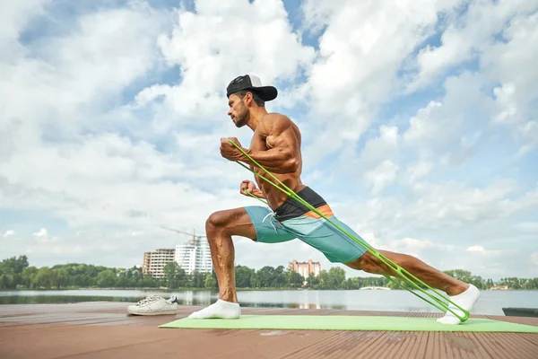 Strong man doing stretching workout in morning near lake. Stock Picture
