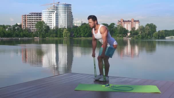 Atletisk och muskulös man stretching gummiband nära sjön — Stockvideo