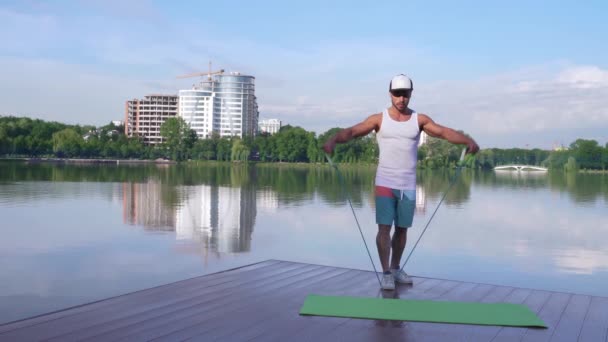 Stark ung kille gör triceps av gummi Expander nära sjön — Stockvideo