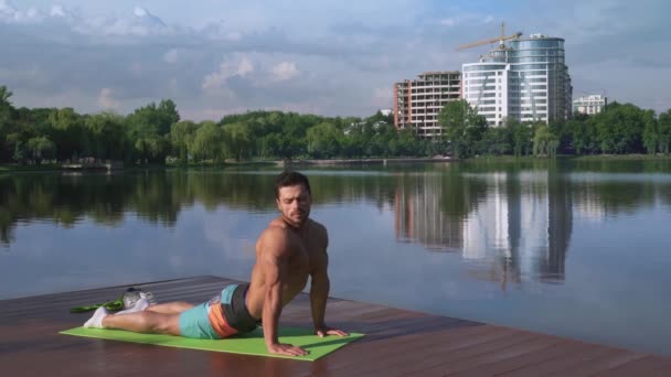 Красивый парень с обнаженной грудью, растягивающий тело на коврике для йоги — стоковое видео