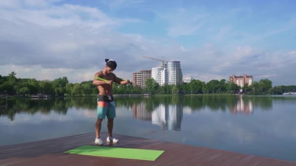 Lago molo con ragazzo muscoloso stretching braccia utilizzando espansore — Video Stock