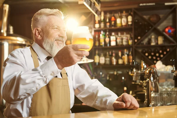 Barman in possesso di bicchiere di birra, in piedi al bancone del bar . — Foto Stock