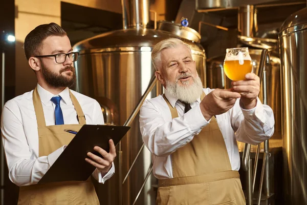 Cerveceros mirando el vaso de cerveza, analizando, escribiendo . — Foto de Stock