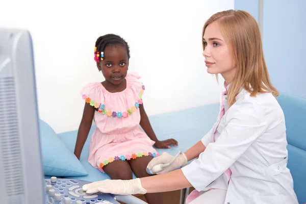 Afro niña sentada en la cama, mientras que el ultrasonido de rodilla unirse . — Foto de Stock